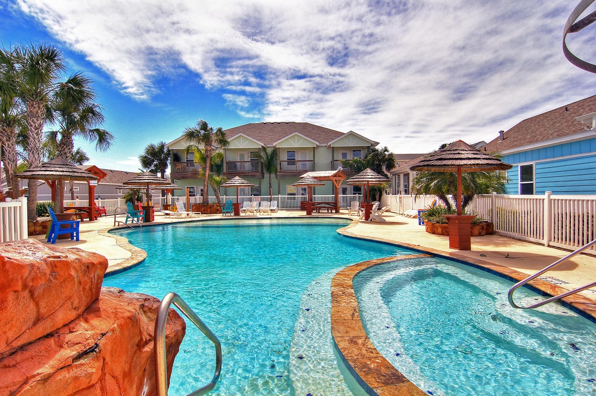 Resort-style pool complex with hot tub, tropical landscaping, and covered cabanas under sunny skies.