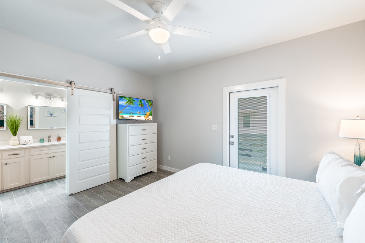 Unwind in your modern bedroom featuring crisp white linens, a calming ceiling fan, and tropical TV views for perfect relaxation.