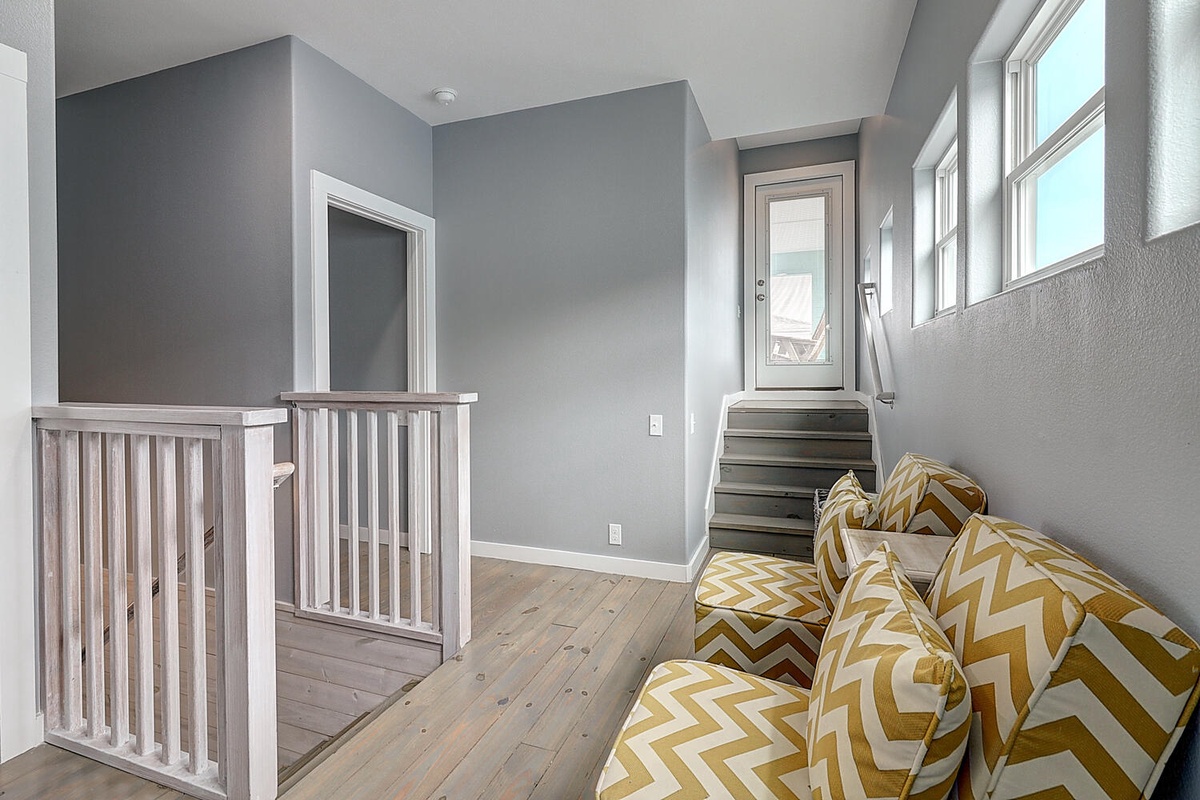 Unwind in this bright upstairs reading nook with cheerful chevron cushions and natural light streaming through tall windows.