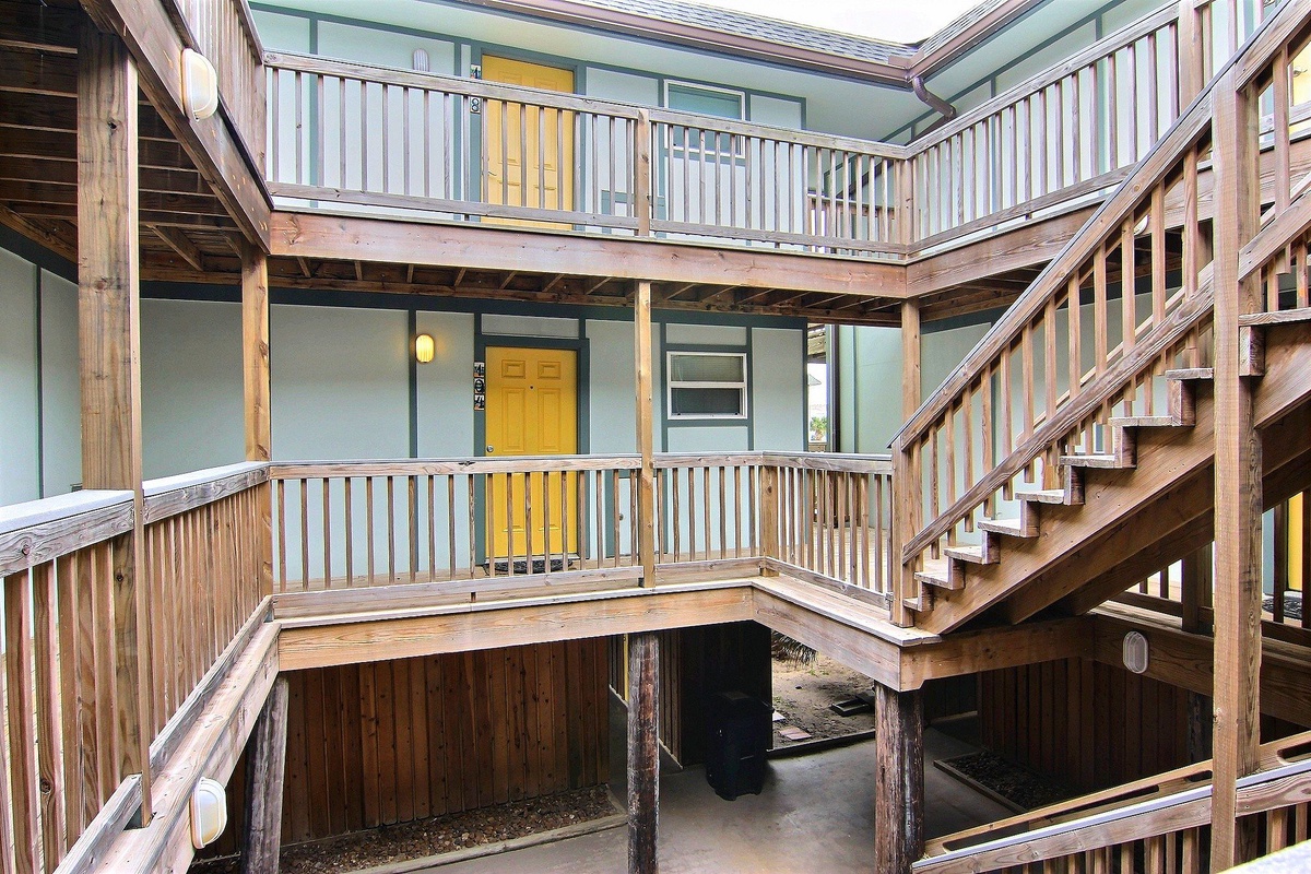 Multi-level property featuring wooden staircases and balconies with bright yellow door accents throughout the courtyard design.