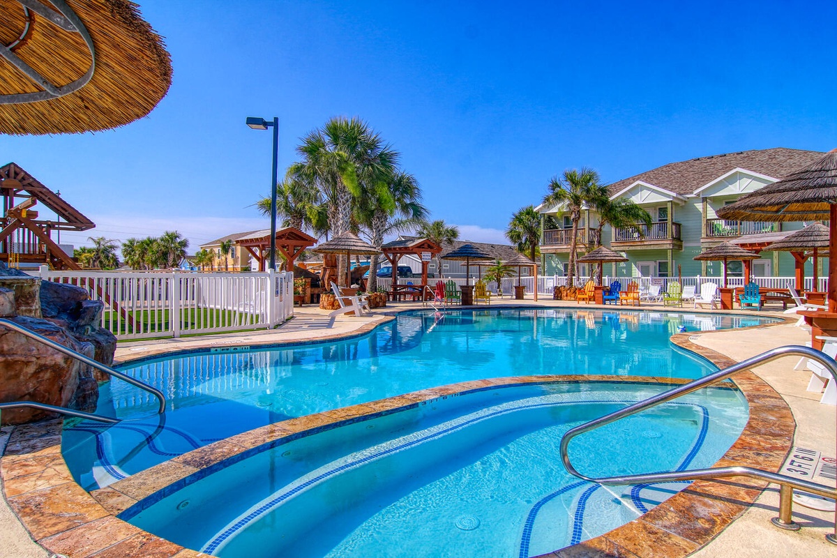 Resort-style pool area with tropical landscaping and multi-story vacation rental buildings surrounding the aquatic facilities.
