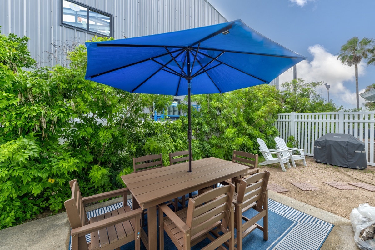 Step onto your private patio where outdoor dining awaits under sunny skies, surrounded by lush greenery and coastal charm.