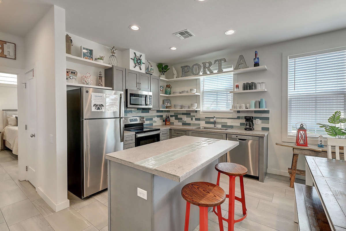Your fully-equipped kitchen invites culinary adventures with stainless steel appliances, granite island, and cheerful red bar stools perfect for morning coffee.