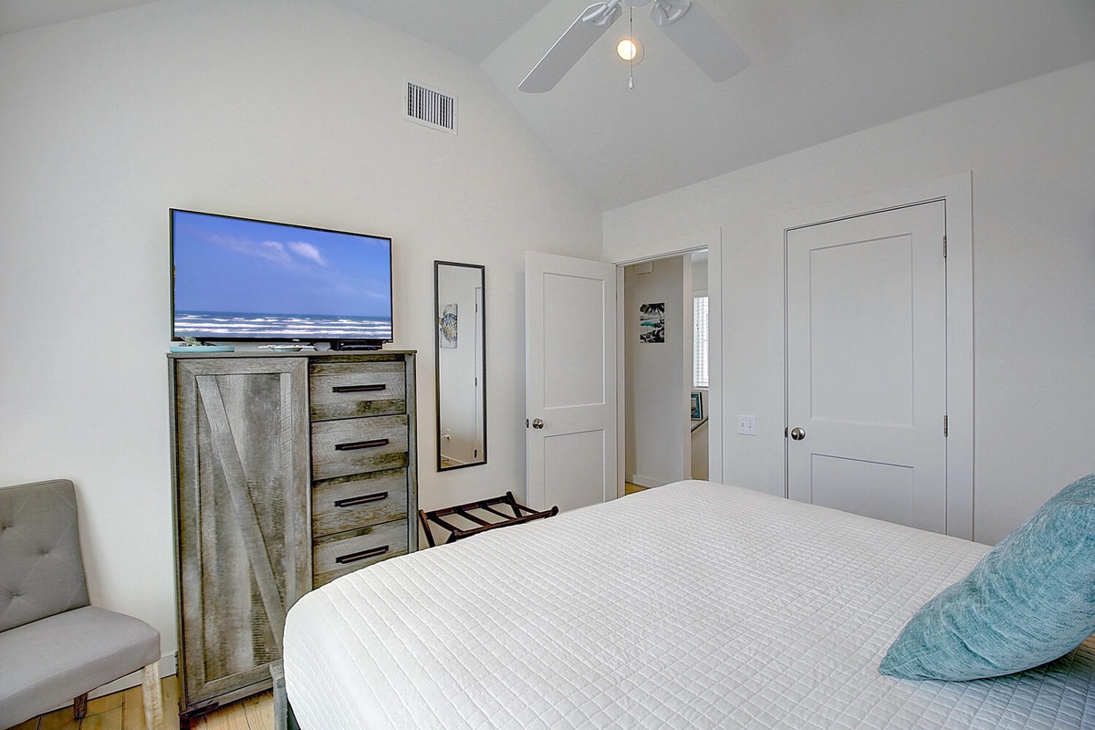 Unwind in your bright, modern bedroom featuring a large TV, rustic-chic dresser, and cozy seating area for ultimate relaxation.