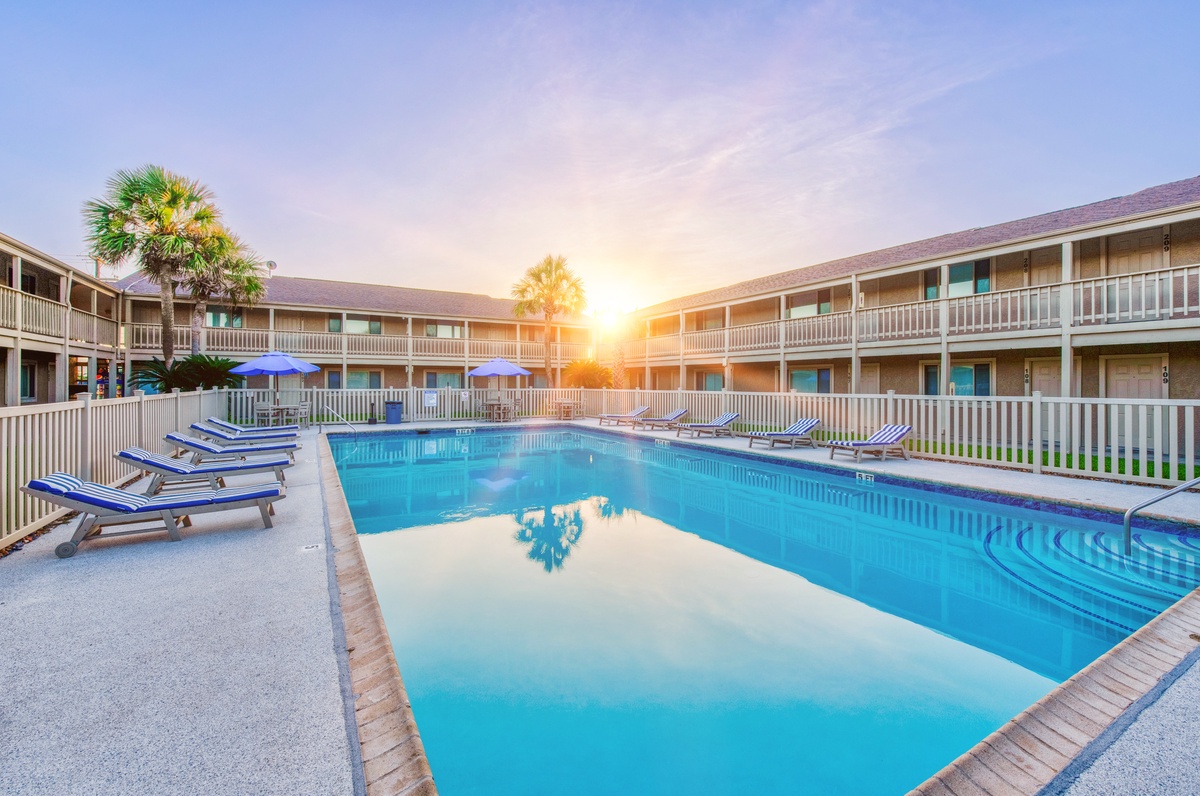 Stunning sunset glow illuminates the pristine pool area surrounded by palm trees and comfortable accommodations.