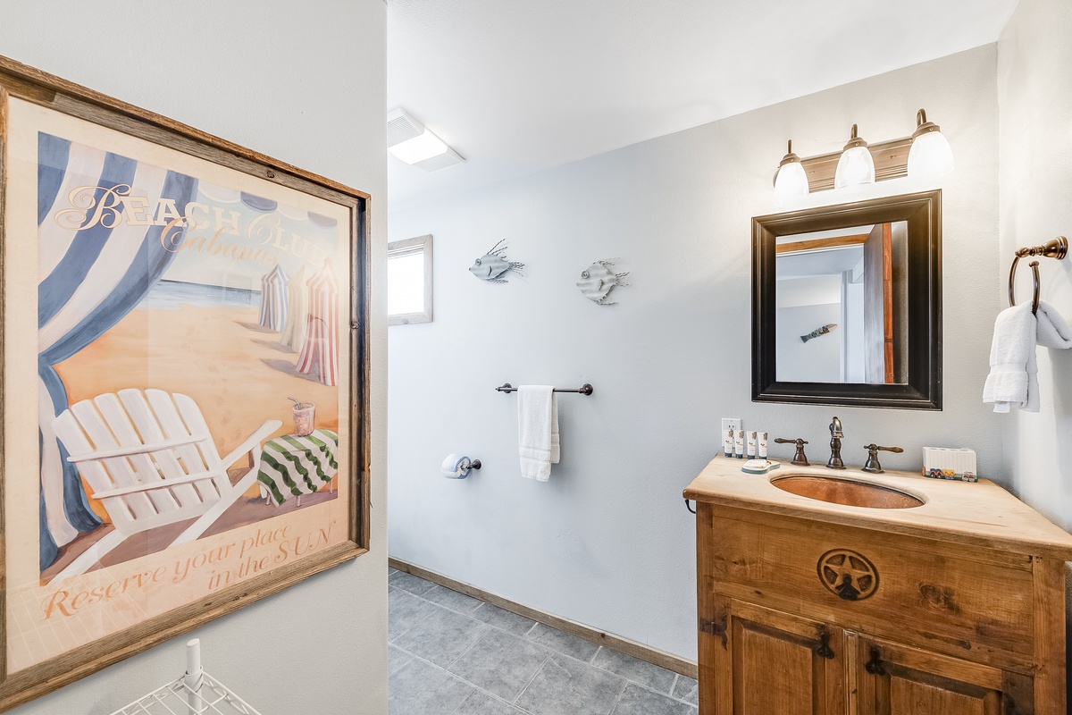 Refresh in your charming coastal-themed bathroom with rustic wood vanity, copper sink, and beachy artwork setting the perfect seaside mood.