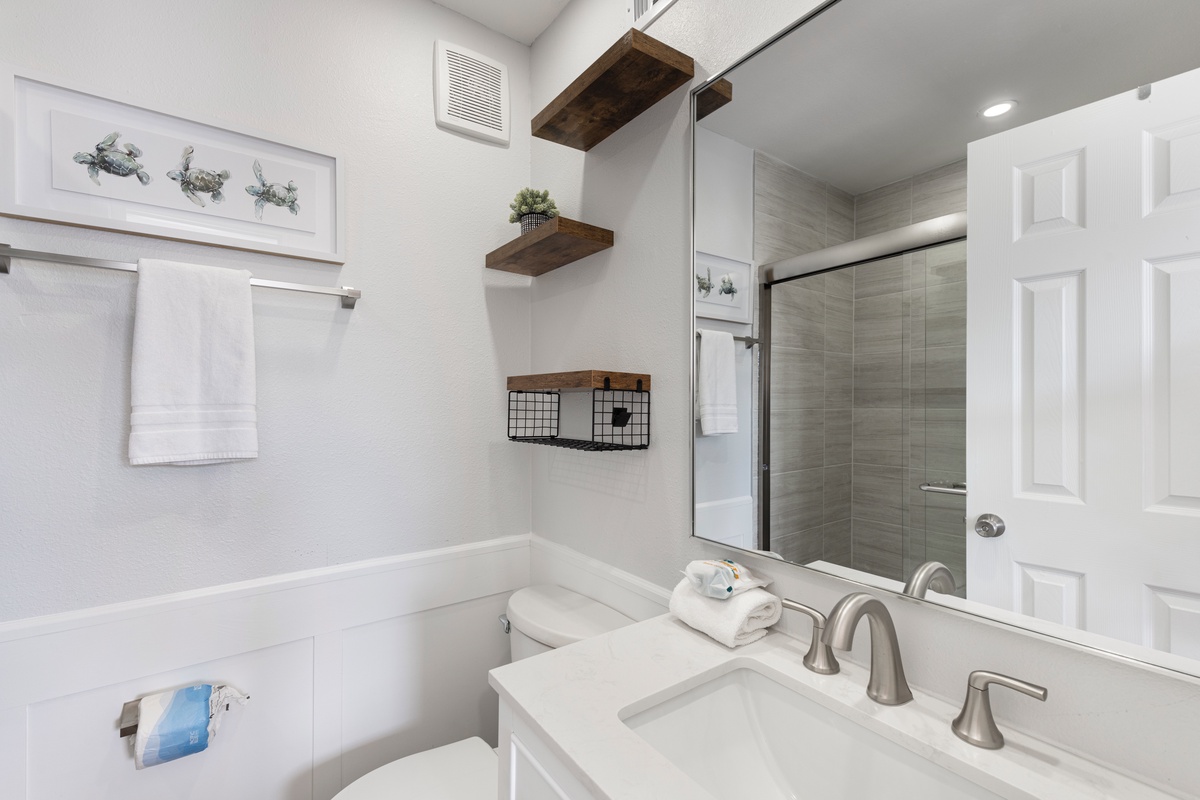 Relax in your bright, modern bathroom with thoughtful touches like fluffy towels, wood shelving, and a spacious shower.