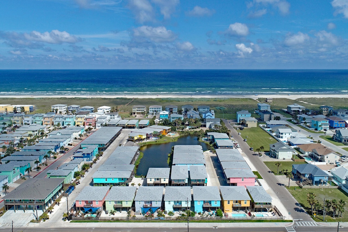 Aerial view of a vibrant beachfront community with colorful rental units just steps from pristine sandy shores and rolling ocean waves.