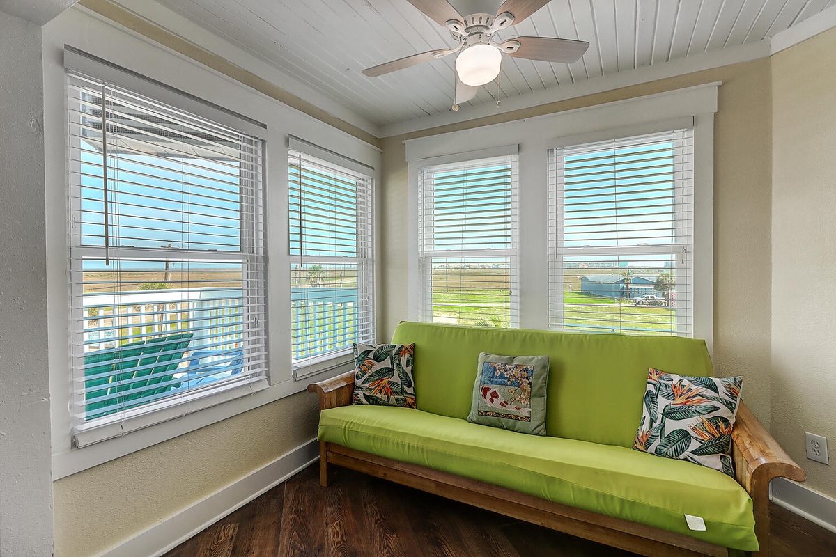 Your bright sunroom features a vibrant green daybed perfect for afternoon relaxation, with panoramic windows framing peaceful countryside views.