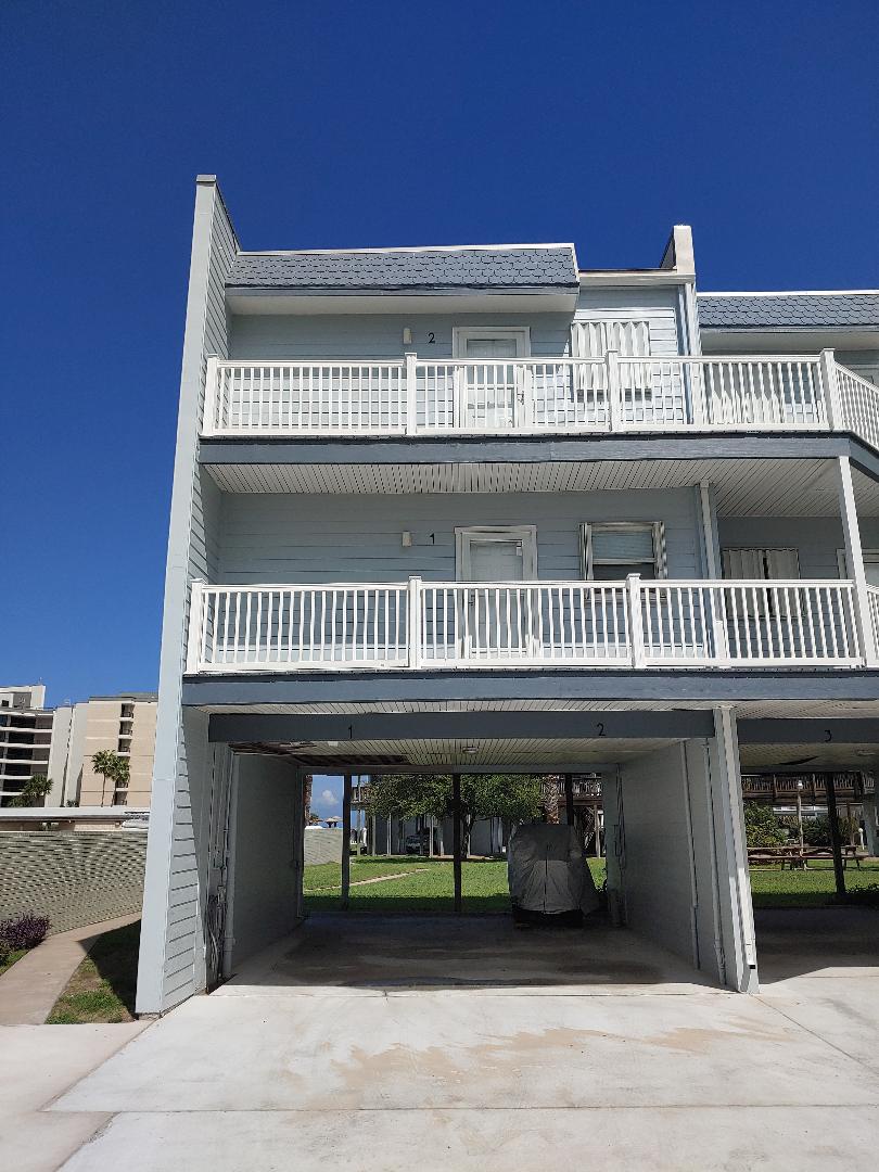 Coastal vacation home with multiple balconies and covered parking beneath clear blue skies.