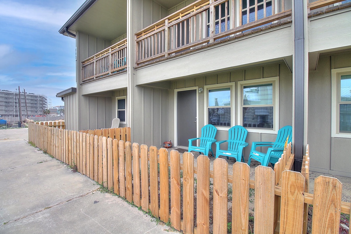 Relax in your private patio with bright blue chairs, perfectly positioned for morning coffee or evening conversations behind a charming picket fence.