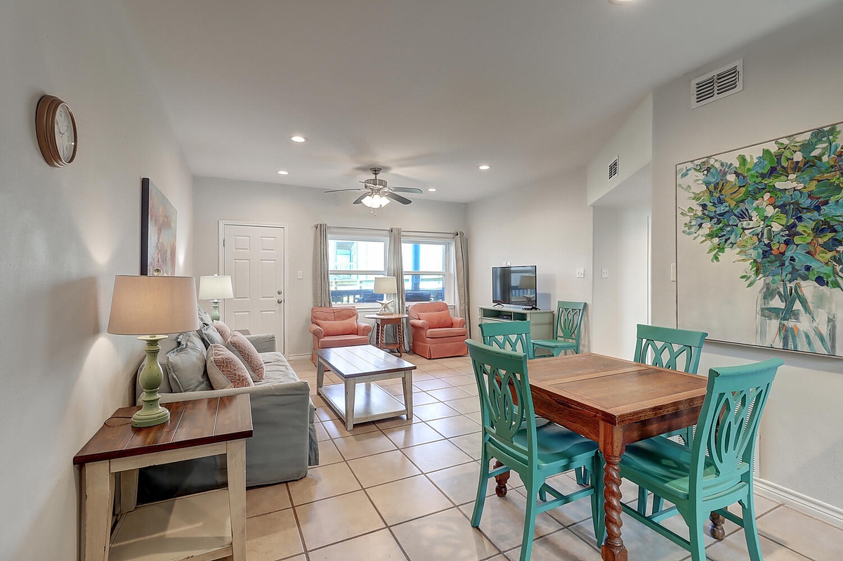 Your open living space blends comfort and coastal charm with turquoise dining chairs, cozy seating, and cheerful artwork creating the perfect gathering spot.