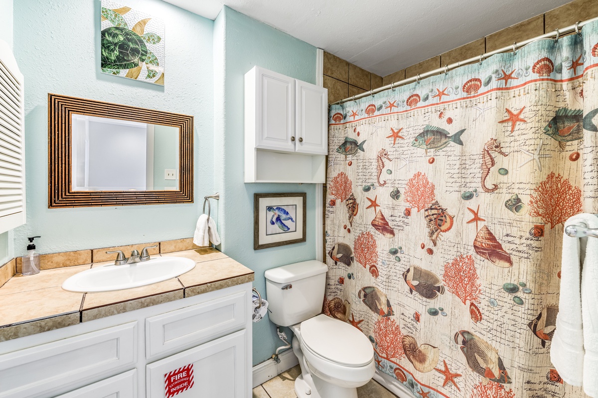 Refresh in your coastal-themed bathroom featuring sea life shower curtain, tiled vanity, and cheerful turquoise walls.