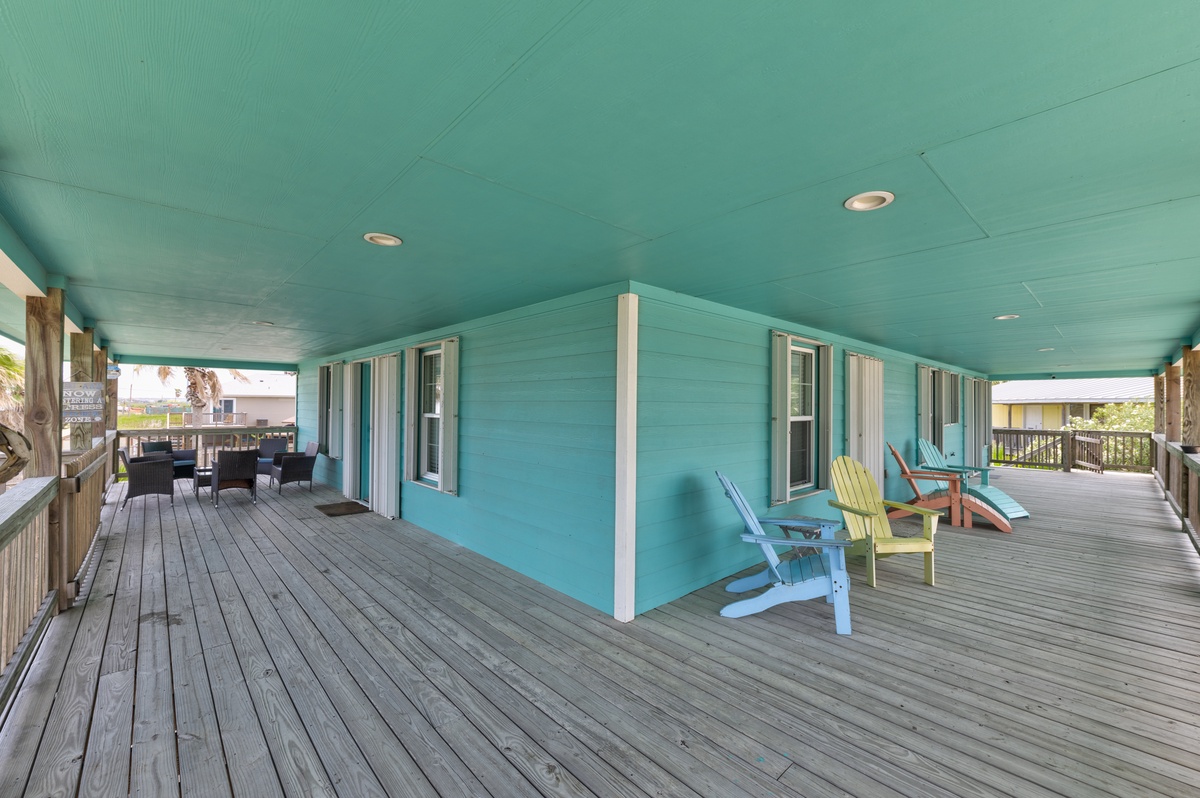 A spacious wraparound deck features vibrant turquoise walls, colorful Adirondack chairs, and covered lounge spaces—perfect for relaxing after a day at the beach.