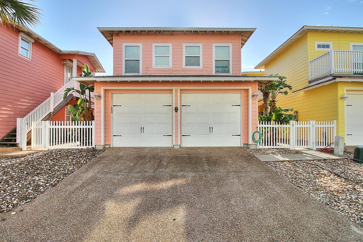 Charming coastal rental home with coral-pink siding and tropical landscaping in a vibrant beachside neighborhood.