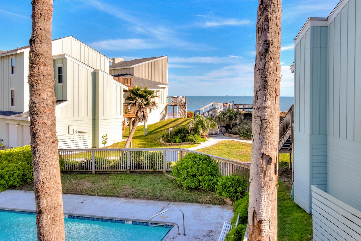Coastal property featuring modern beach homes, palm trees, pool area, and scenic walkway leading to waterfront access.