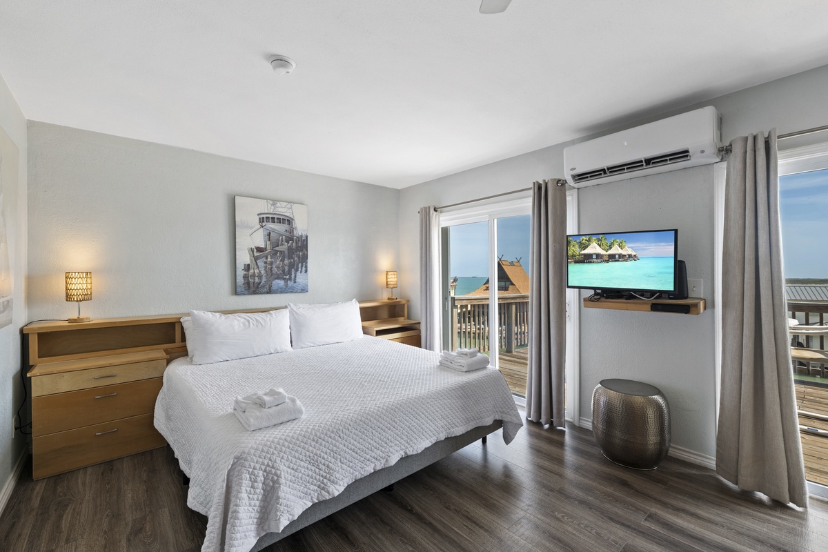 Your bright bedroom offers modern comfort with crisp linens and ocean views beyond your private balcony doors.
