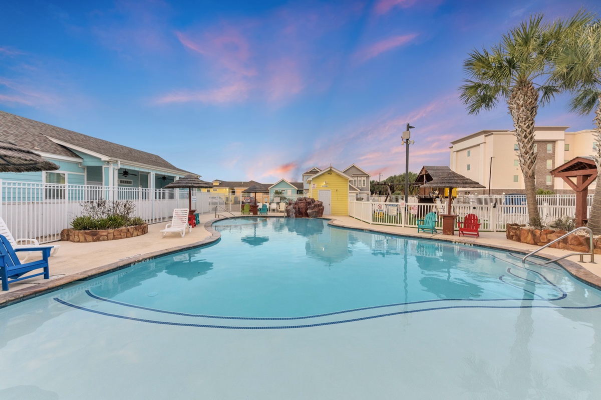 Dive into your tropical escape with this stunning pool area surrounded by colorful beach cottages under painted skies.