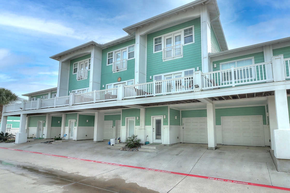 Charming coastal townhomes with bright green siding, private balconies, and covered parking create the perfect beach getaway setting.