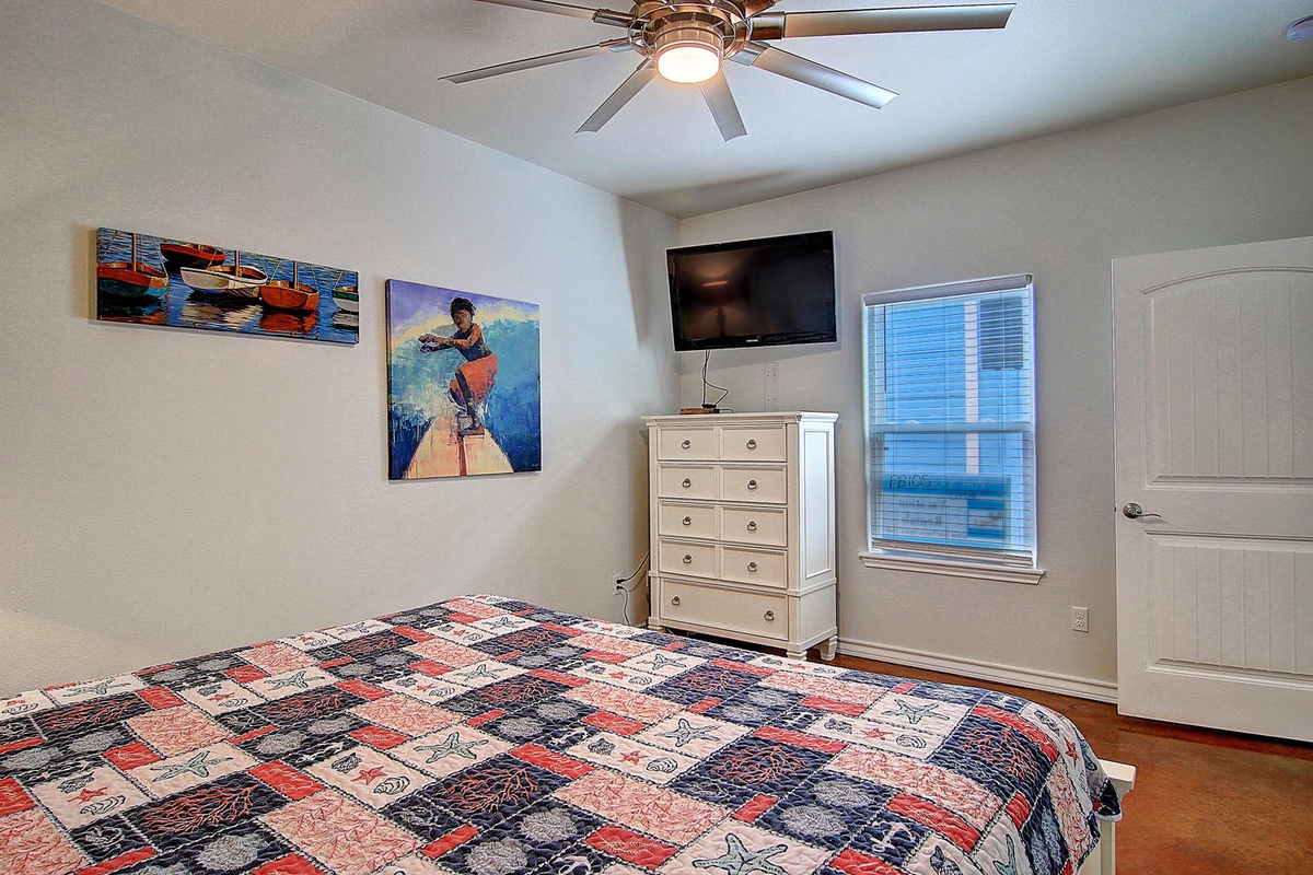Relax in your peaceful bedroom with nautical art, ceiling fan comfort, and TV entertainment for cozy evenings.