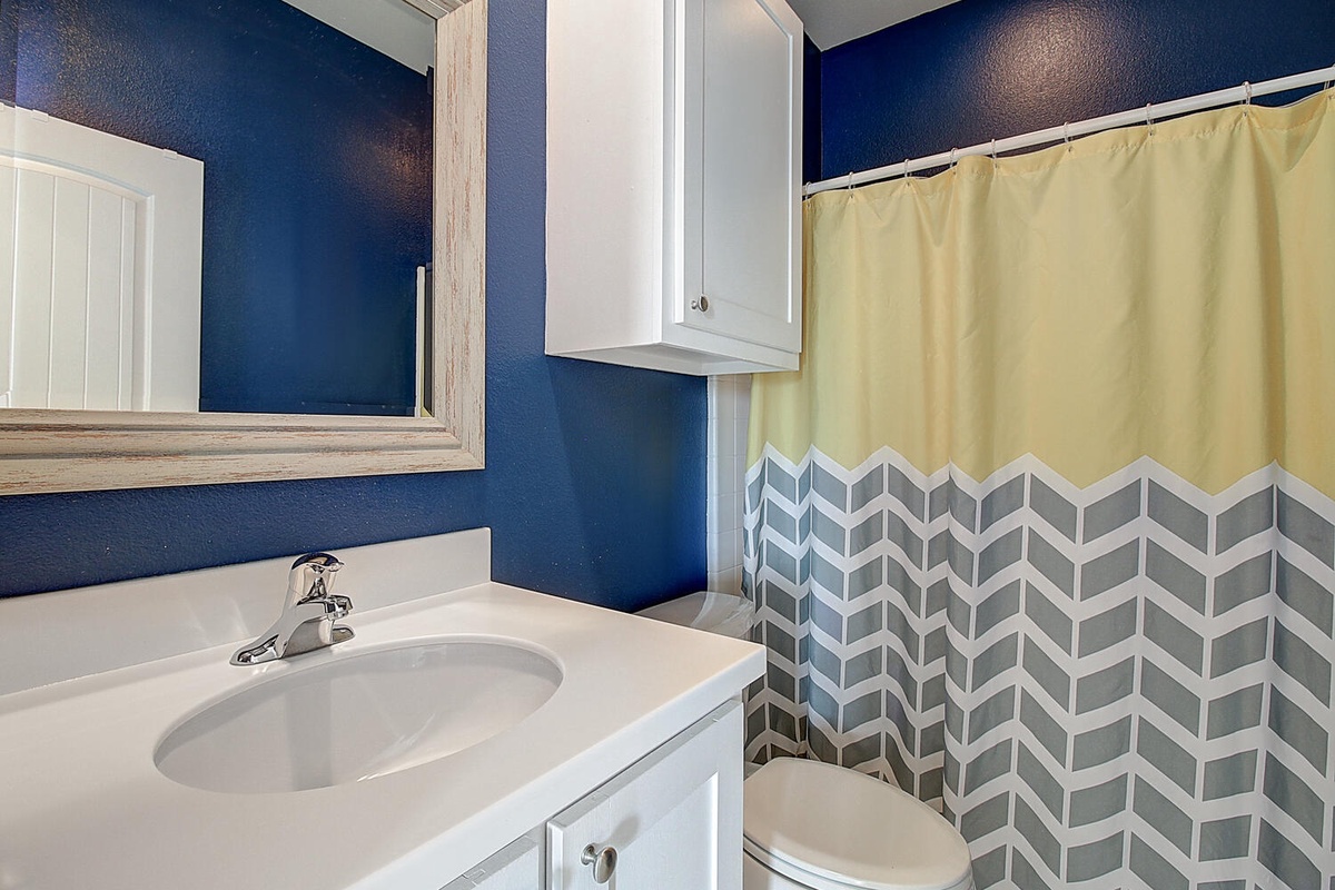 Your stylish bathroom features bold navy walls, crisp white vanity, and cheerful chevron shower curtain for a fresh, modern feel.
