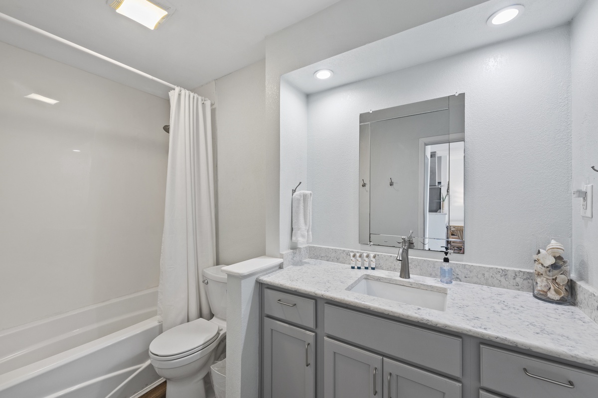 Unwind in your pristine bathroom featuring elegant marble countertops, modern gray cabinetry, and a spacious tub-shower combo.