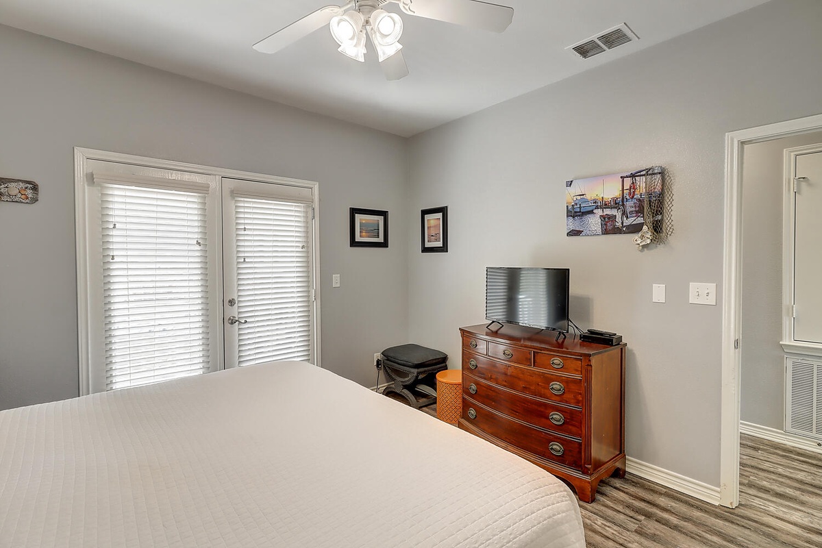 Relax in your peaceful bedroom featuring a plush bed, elegant cherry dresser with flat-screen TV, and French doors opening to your private outdoor space.