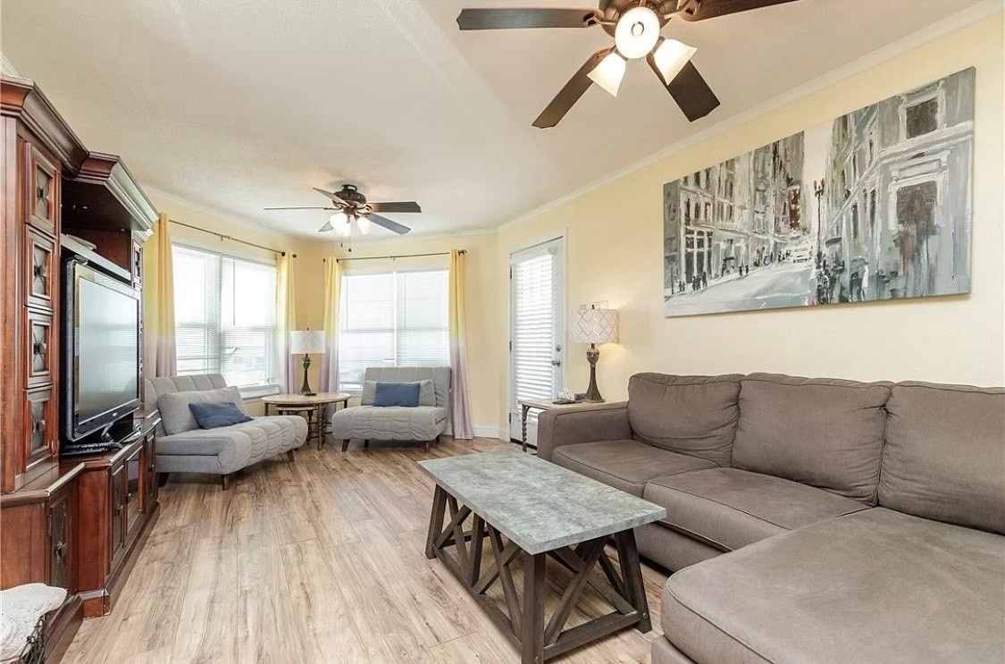 Relax in this bright, airy living space with plush seating, entertainment center, and natural light from corner windows—your perfect home base.