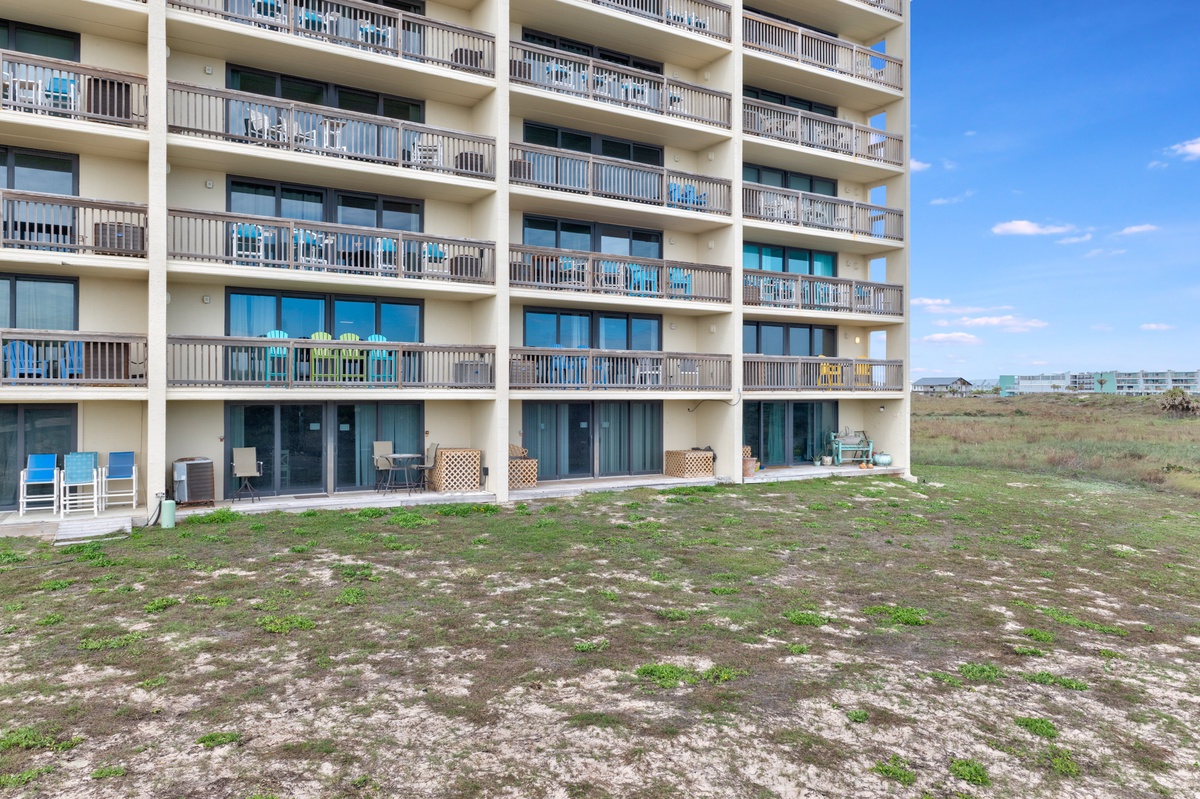 Multi-story beachfront building with private balconies and ground-floor patios overlooking open coastal landscape under clear blue skies.