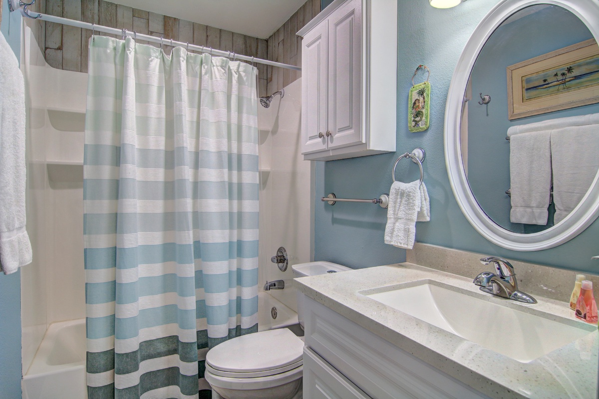 Refresh in your coastal-themed bathroom with calming blue walls, striped shower curtain, and fresh towels awaiting your arrival.