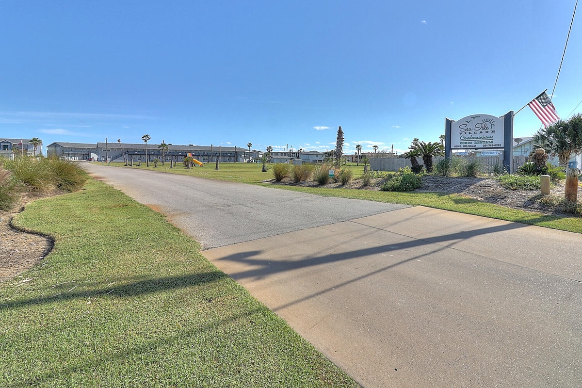 Peaceful residential area entrance with property signage and well-maintained landscaping under clear blue skies.