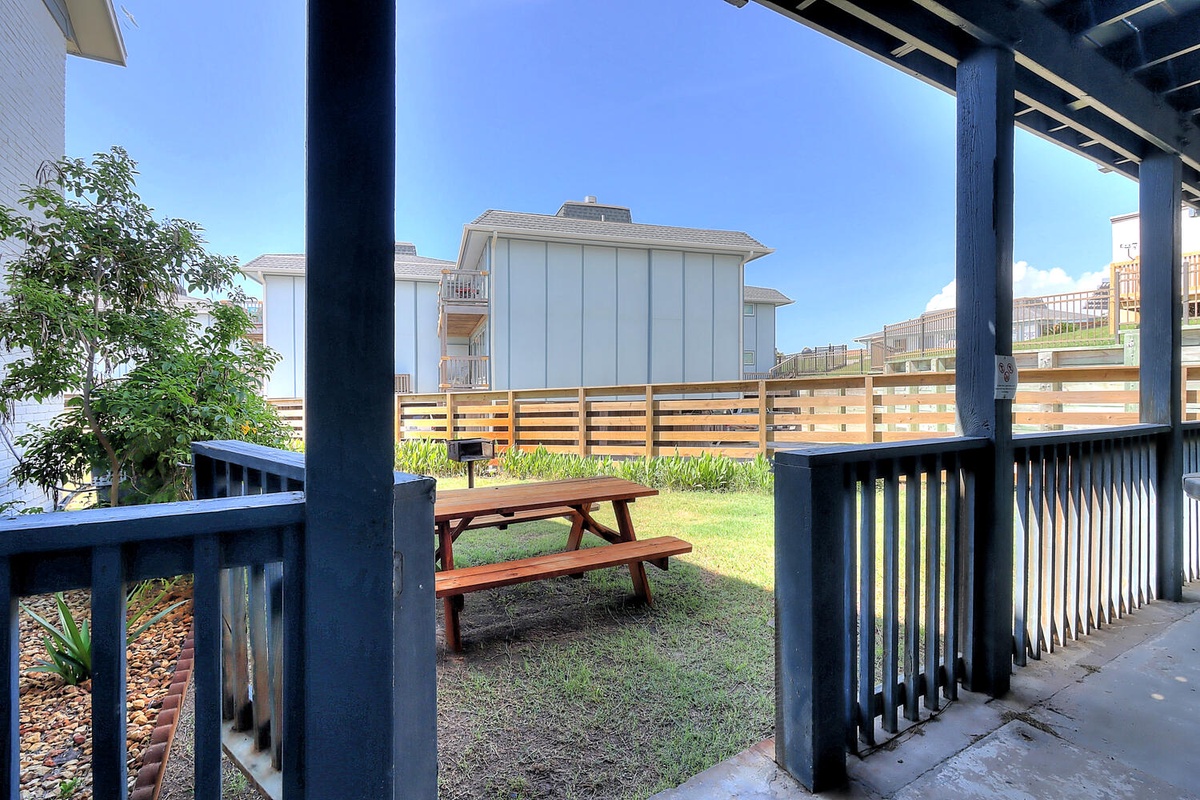 Step onto your private patio where a peaceful picnic table awaits, framed by lush green grass and thoughtful landscaping.