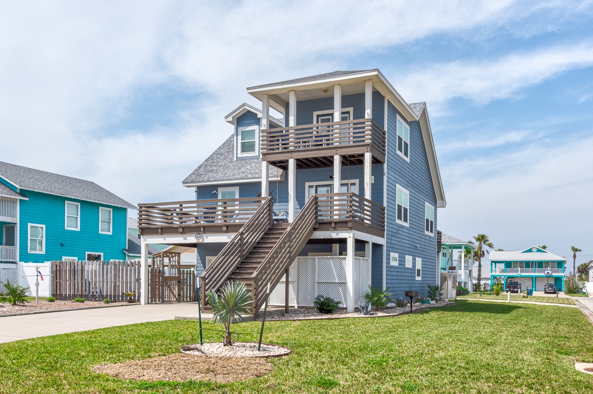 A charming coastal vacation home with multiple levels and outdoor deck space, surrounded by colorful beach community properties.