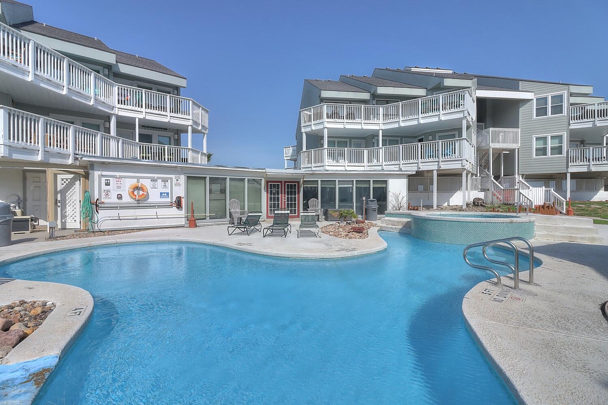 Multi-level beach property with curved swimming pool featuring spa, surrounded by modern coastal buildings and private balconies.