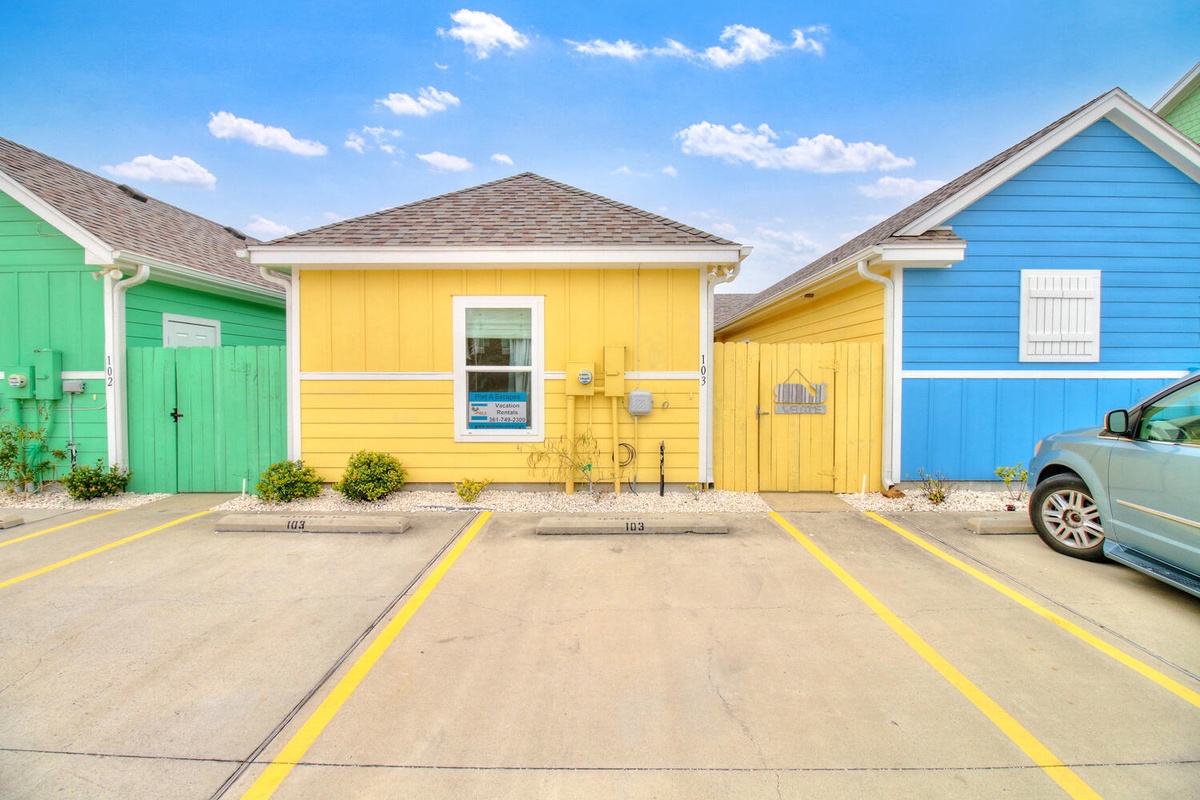 Vibrant beach house row with designated parking spaces creates a cheerful coastal atmosphere under bright blue skies.
