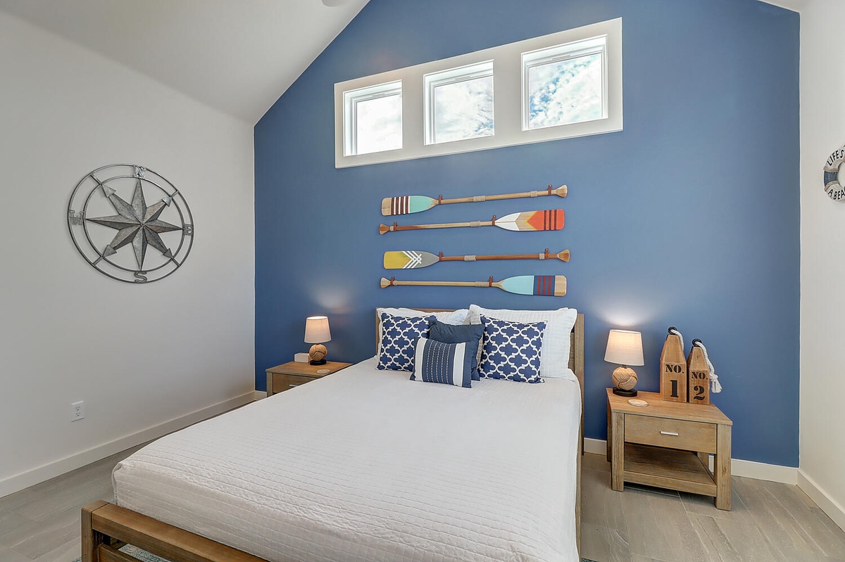 Drift off to sleep in your nautical-themed bedroom, where colorful oar wall art and coastal blue hues create a peaceful seaside retreat.