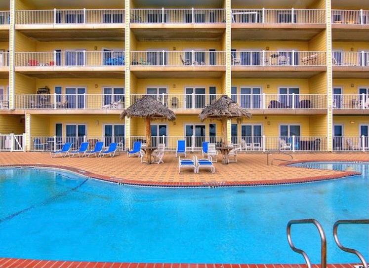 Sparkling blue pool with tropical thatched umbrellas and sunny yellow balconies create the perfect vacation backdrop.
