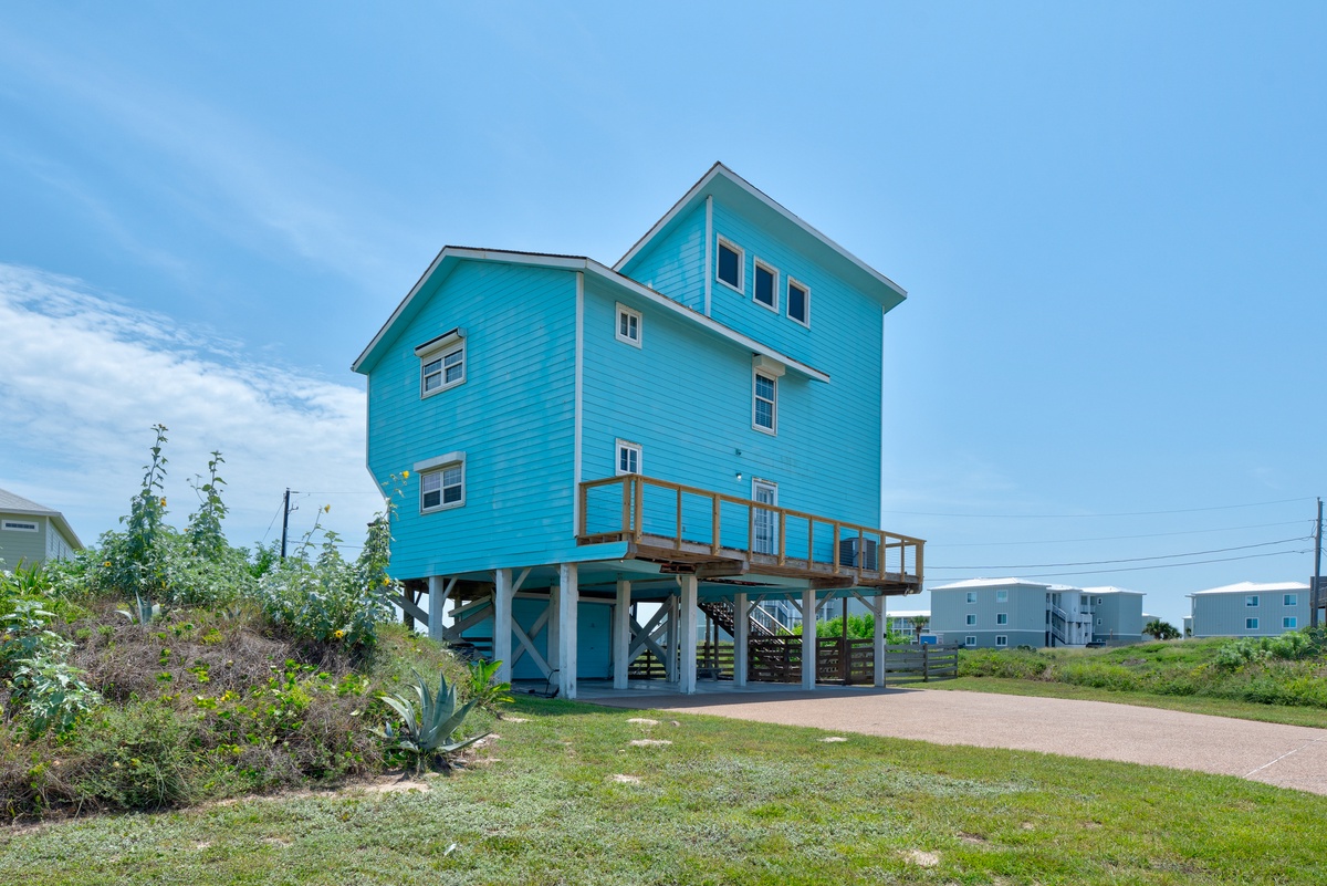 Coastal beach house on stilts with covered parking below and an elevated deck.