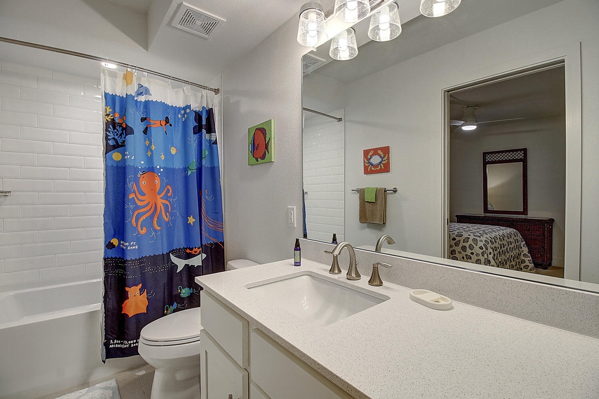Step into your bright bathroom featuring a tub-shower combo with playful ocean-themed curtain, modern vanity, and cheerful wall art.