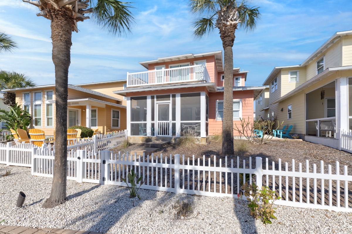 Charming coastal cottage with screened porch and rooftop deck surrounded by swaying palms in a peaceful beachside neighborhood.