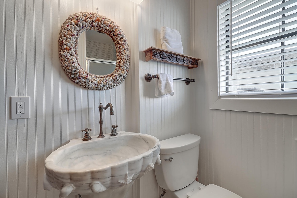 Your coastal-inspired powder room welcomes you with charming seashell details and fresh white linens for a refreshing seaside retreat.