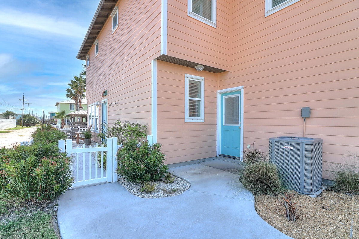 Charming coastal property with tropical landscaping and bright turquoise door welcomes guests to their beachside retreat.