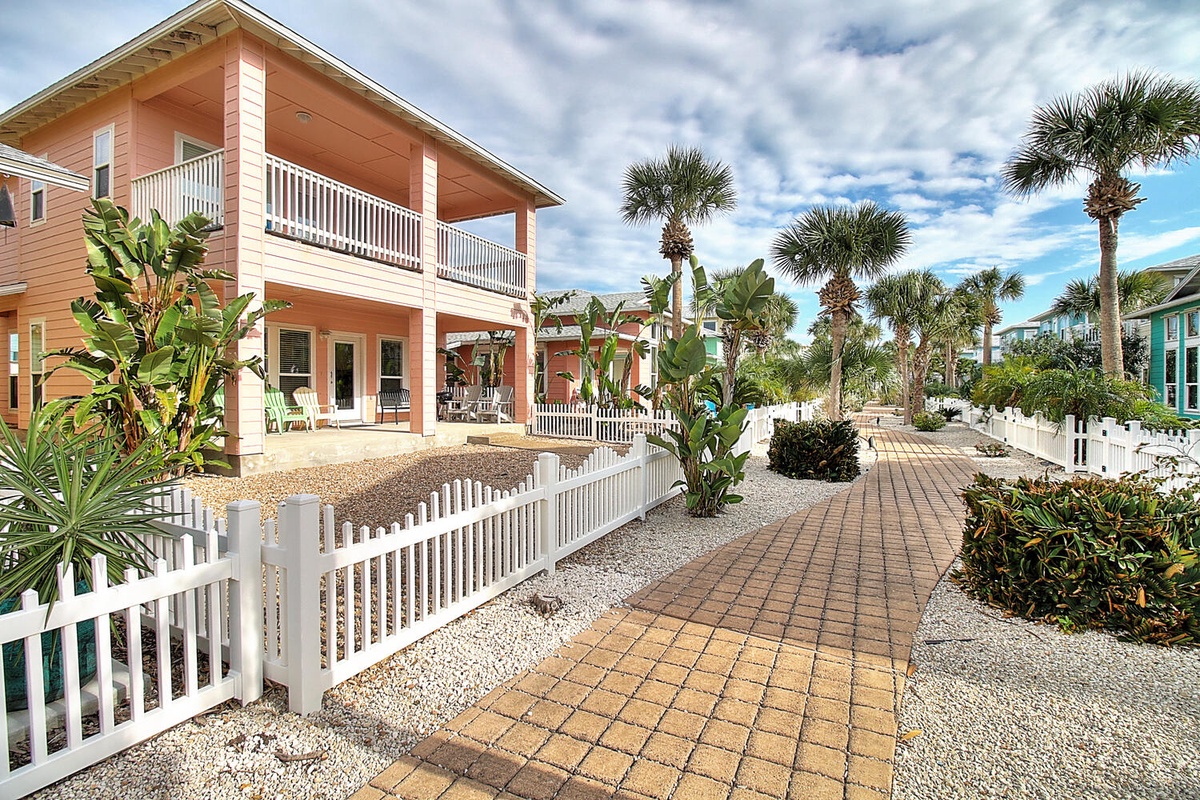 Coastal cottage with tropical landscaping and brick walkway in a charming beachside neighborhood.
