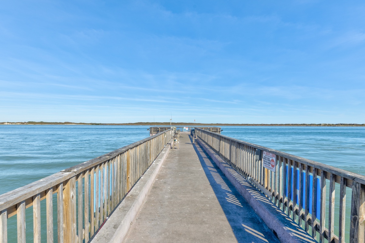 Wooden fishing pier extends into pristine blue waters under expansive coastal skies near the property.