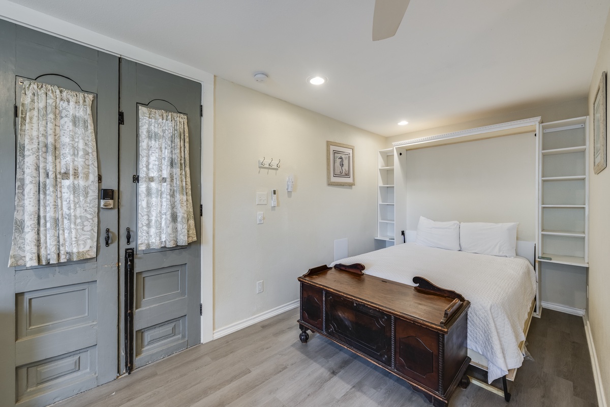 Your cozy bedroom features a comfortable queen bed, charming vintage chest, and thoughtful built-in shelving. Relax in the soft lighting and enjoy the unique character of the antique-style doors.