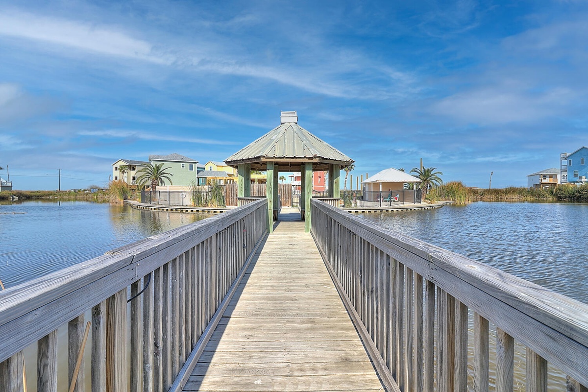 Wooden pier leads to charming waterfront pavilion surrounded by colorful coastal homes and swaying palms.