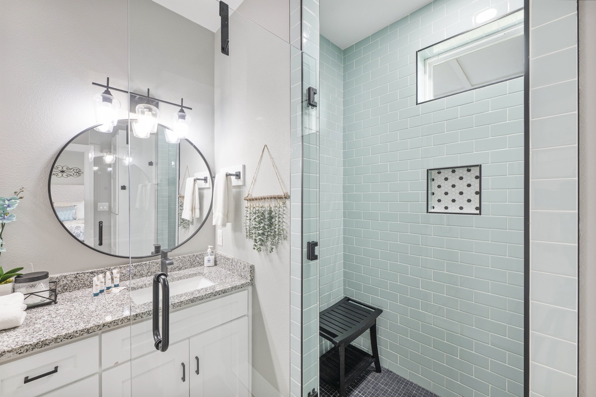 Refresh in your spa-like bathroom featuring a spacious glass shower with mint subway tiles and modern vanity with granite countertops.