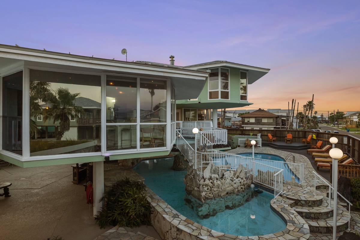 Stunning sunset views illuminate this waterfront property featuring a curved pool with decorative rock features and elegant outdoor lounging areas.