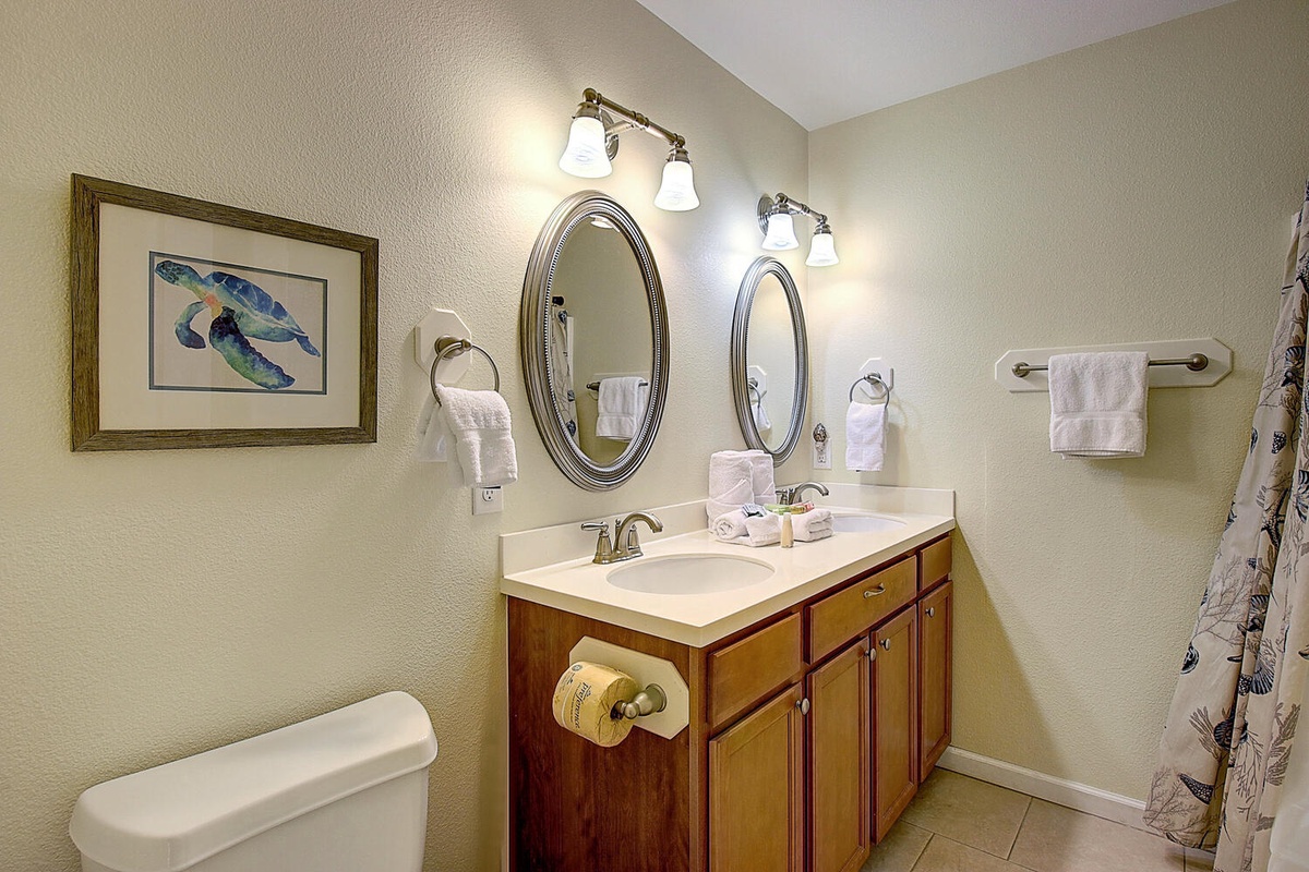 Freshen up in your spacious bathroom featuring double vanities, warm wood cabinetry, and coastal artwork that creates a serene retreat.