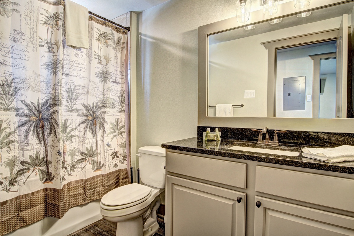 Step into your elegant bathroom featuring a tropical palm shower curtain, granite counters, and thoughtful vanity lighting for your daily routines.